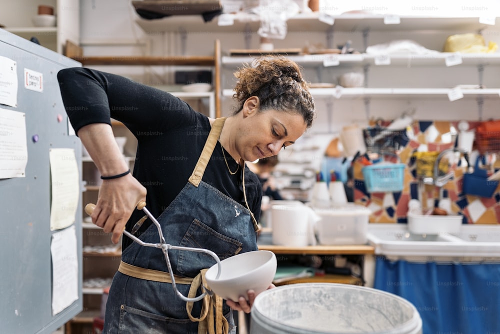 Stock photo of concentrated woman in apron working in pottery atelier.