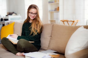A happy young female student sitting on sofa, studying. Copy space.