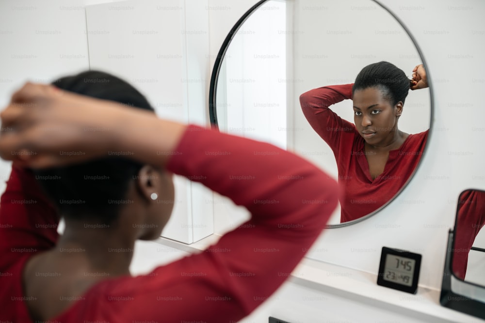 髪を直し、バスルームの鏡を覗き込むアフリカの黒人女性の喪服のルーチン。ヘアスタイリングと準備