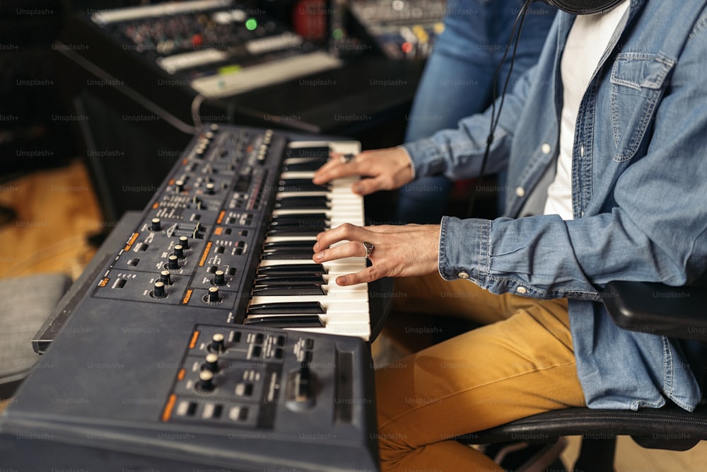 Stock photo of unrecognized musician in professional music studio playing electronic piano keyboard.