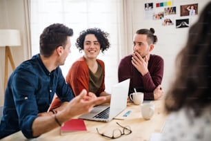 A group of young cheerful friends with laptop sitting at table indoors, house sharing concept.