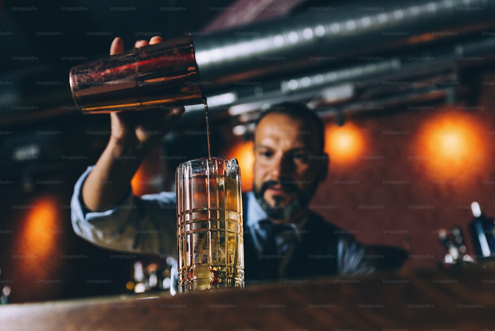 Expert barman is making cocktail at night club.