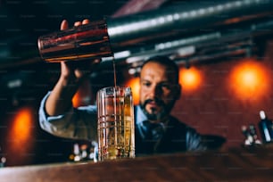 Expert barman is making cocktail at night club.