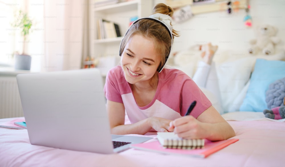 Young female student with laptop lying on bed, online lesson concept.