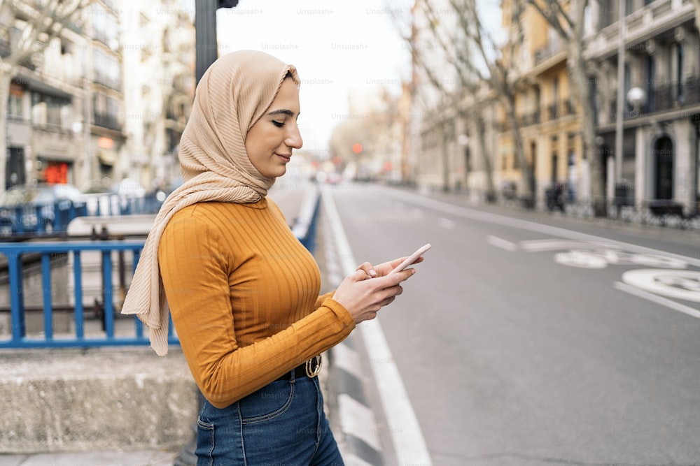 Bella giovane donna musulmana che indossa il velo usando il suo telefono cellulare per strada.