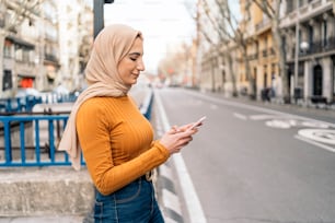 Bonita joven musulmana con pañuelo en la cabeza usando su teléfono móvil en la calle.