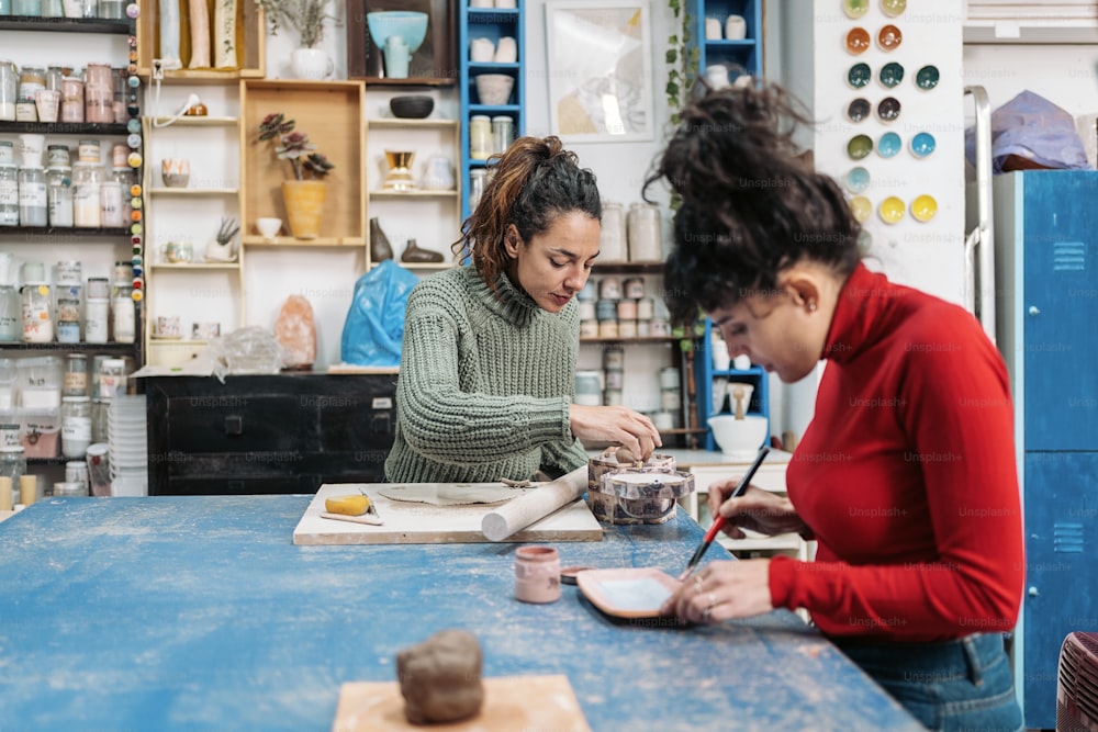 Stock photo of two happy women in apron using clay during pottery class.