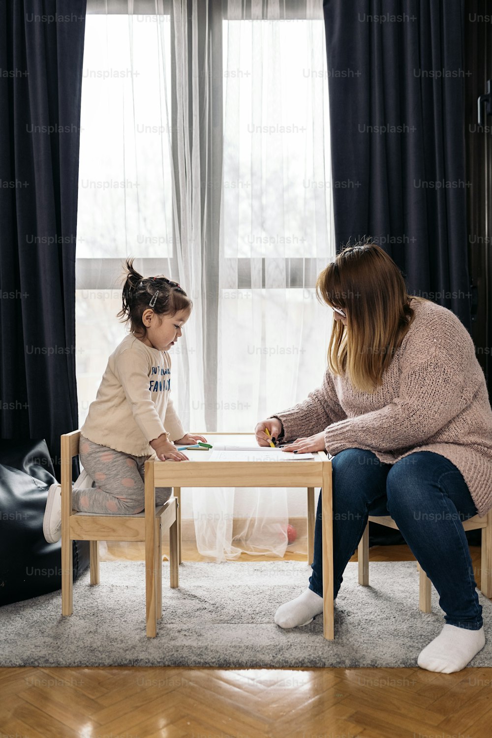 Stock photo of happy woman doing drawings in the living room with her cute daughter.
