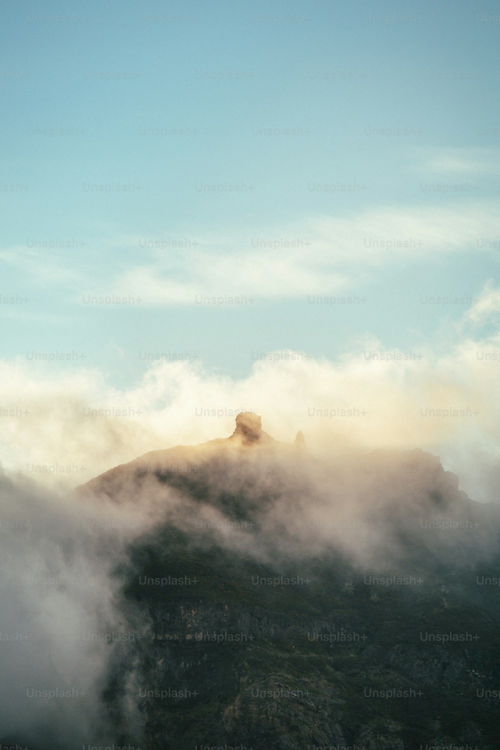 a mountain covered in fog and clouds under a blue sky