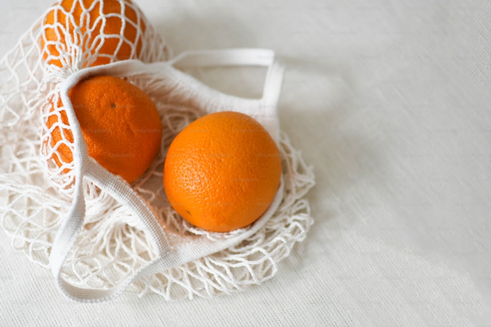 Dos naranjas en una bolsa blanca sobre un paño blanco