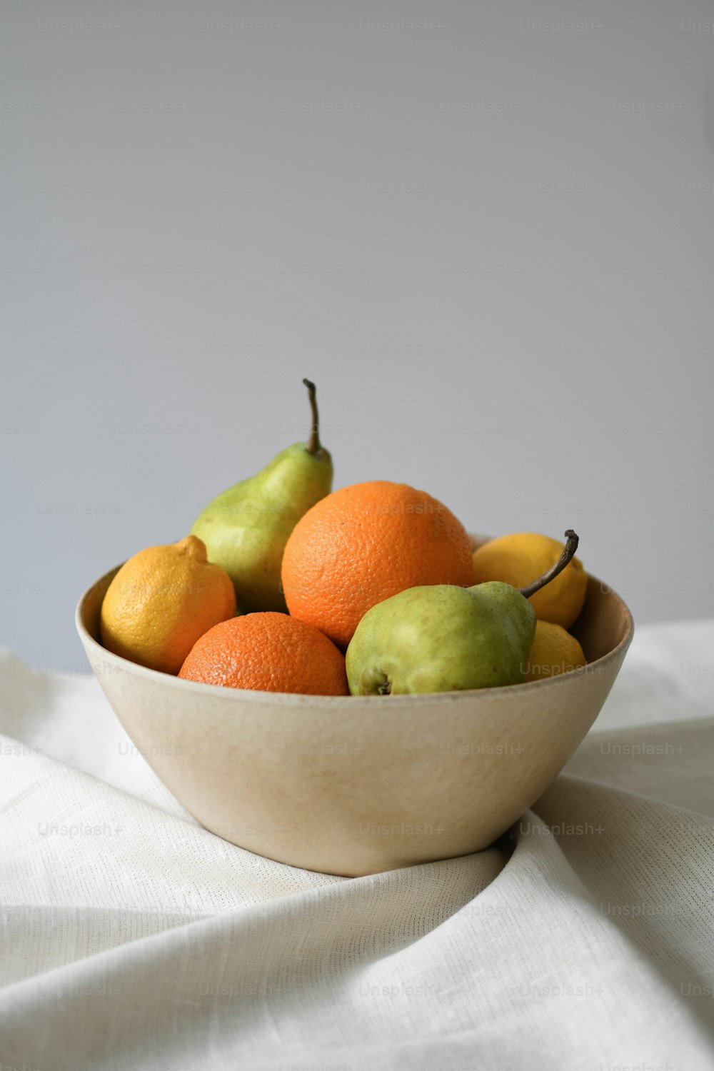 eine Schüssel mit Orangen und Birnen auf einem weißen Tuch