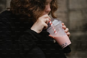 Una mujer bebiendo una bebida rosa de un vaso de plástico
