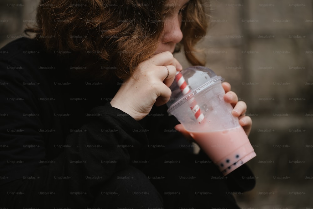 uma mulher bebendo uma bebida rosa de um copo de plástico