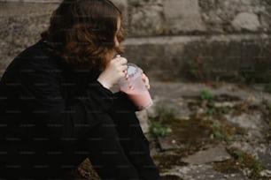 a woman sitting on the ground drinking from a pink cup