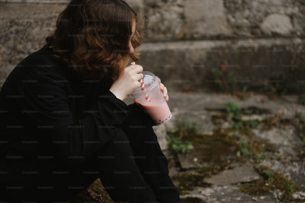 Una mujer sentada en el suelo bebiendo de una taza rosa