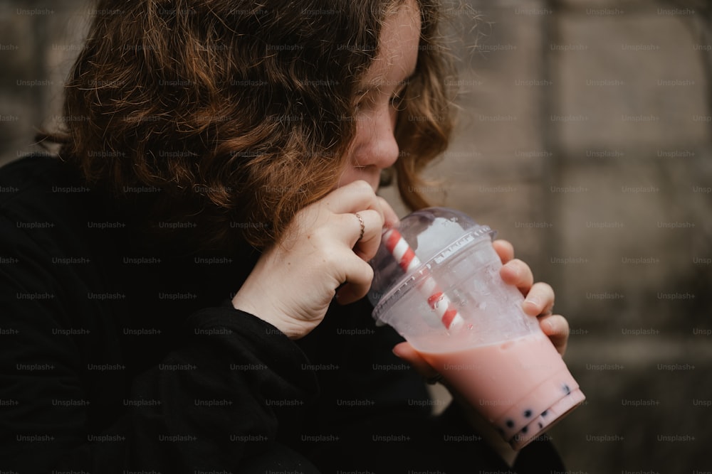 uma mulher bebendo um smoothie rosa de um copo de plástico