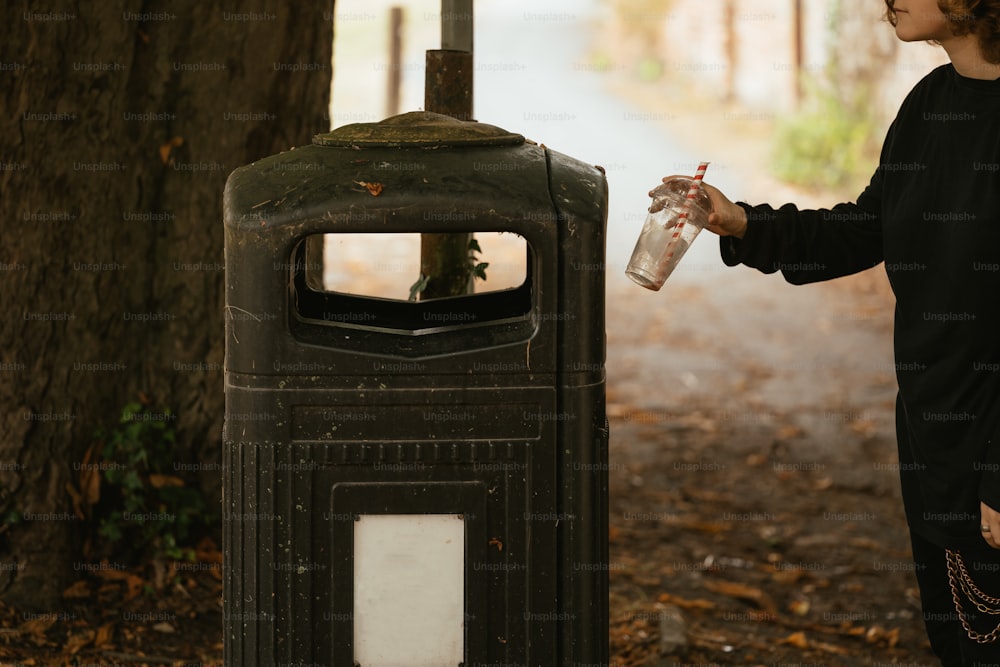 Una mujer parada junto a un bote de basura