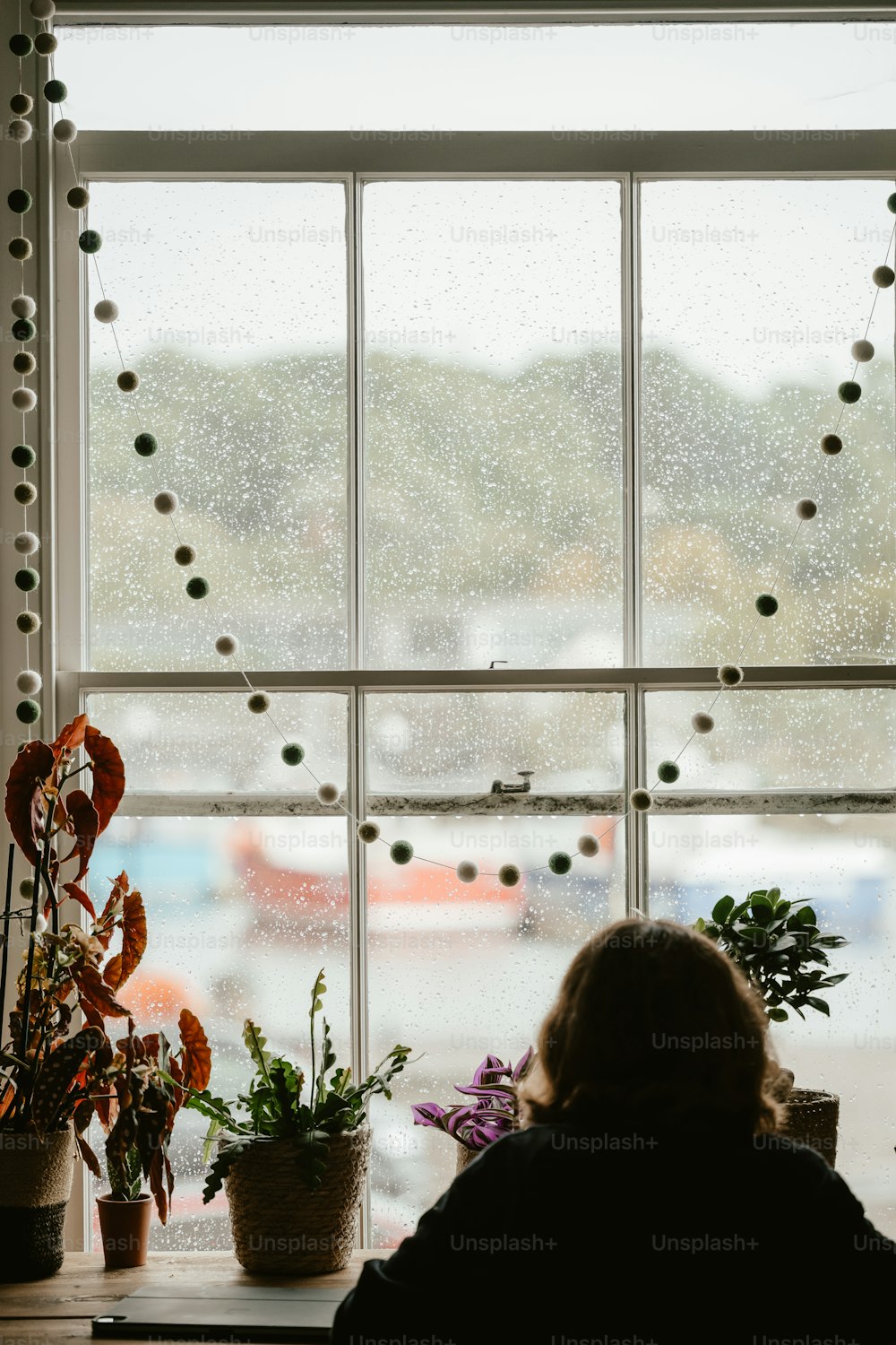uma mulher sentada em frente a uma janela ao lado de um vaso de planta