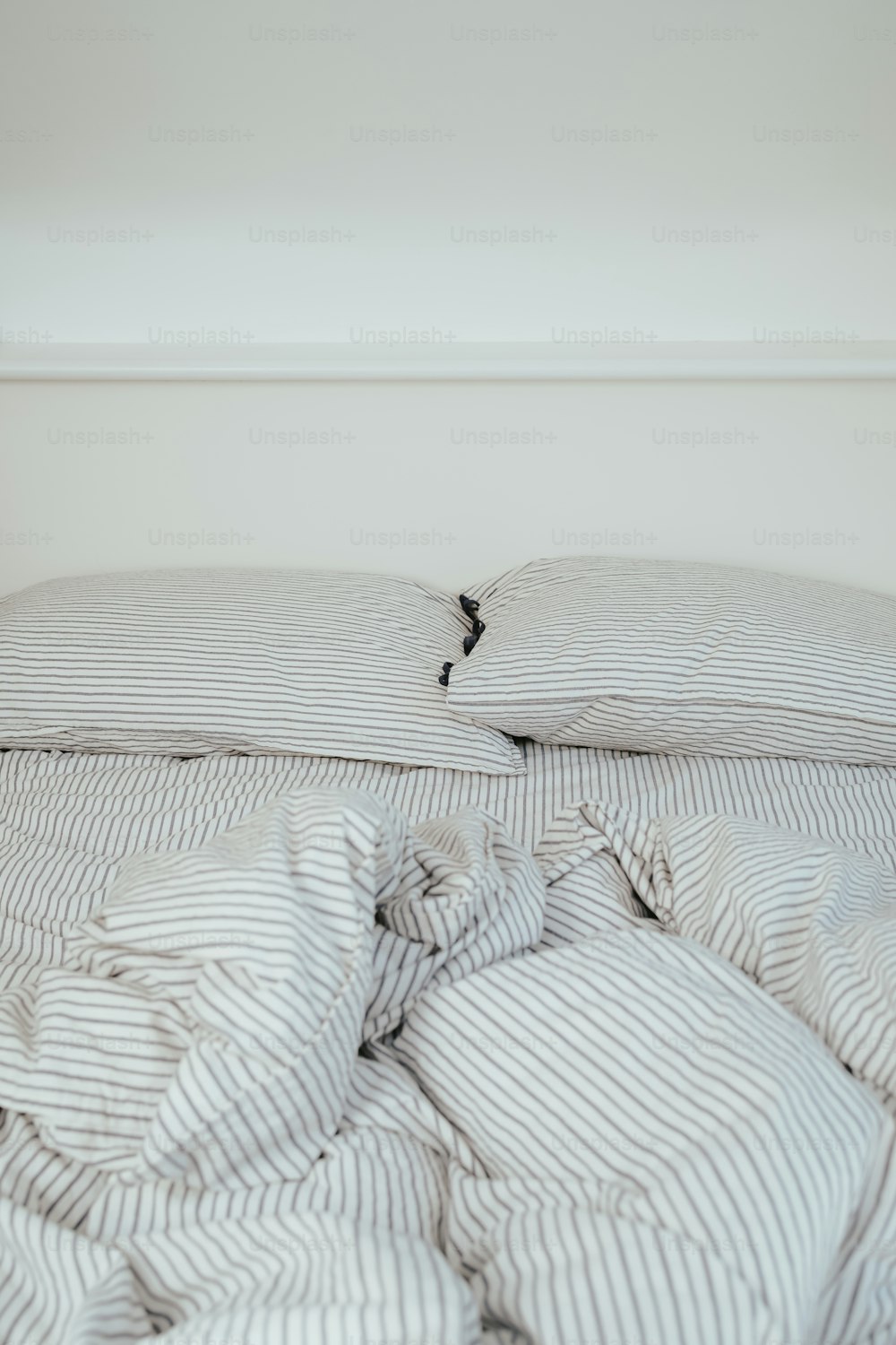 un lit défait avec une couette rayée et des oreillers