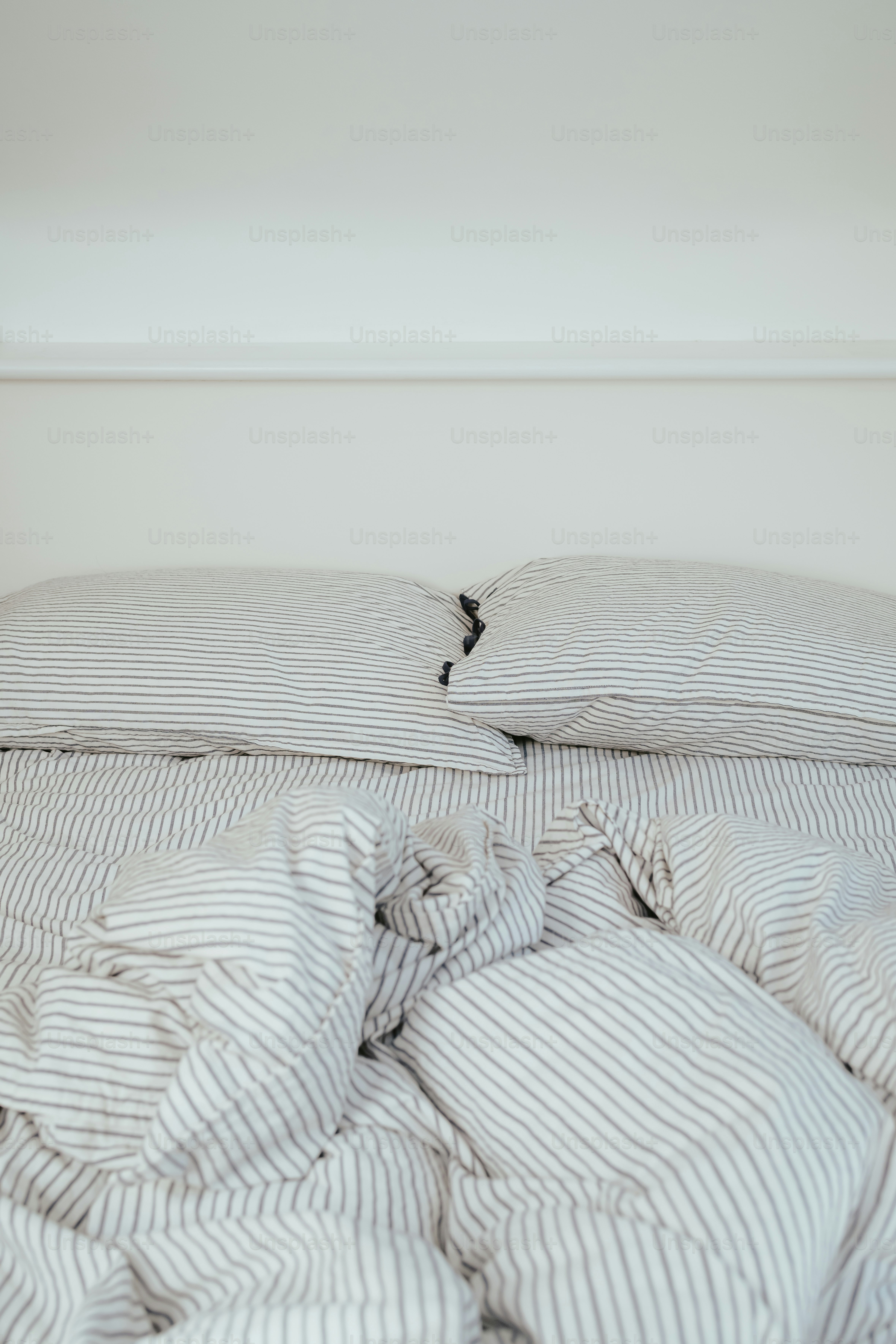 an unmade bed with a striped comforter and pillows