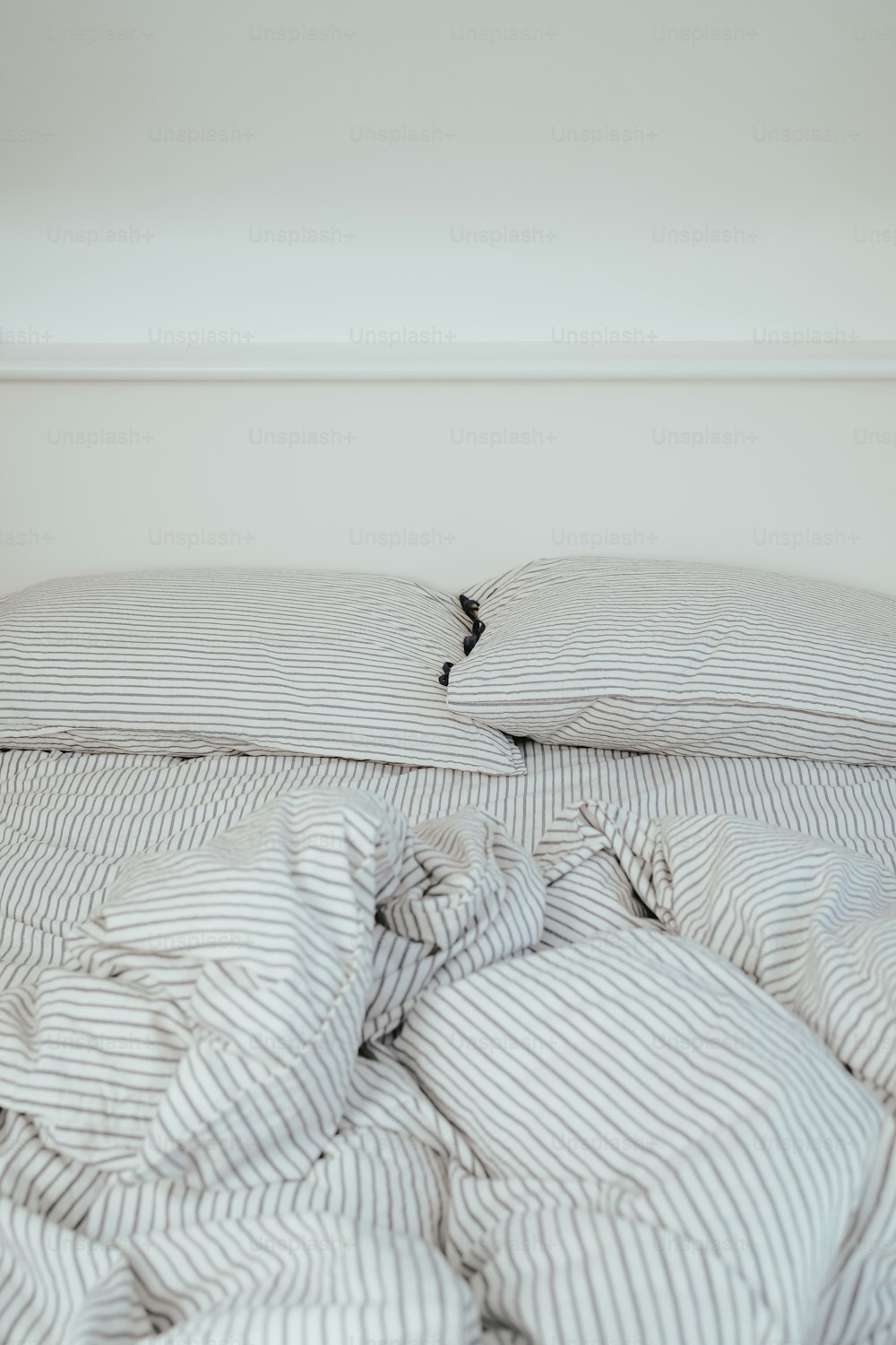 an unmade bed with a striped comforter and pillows