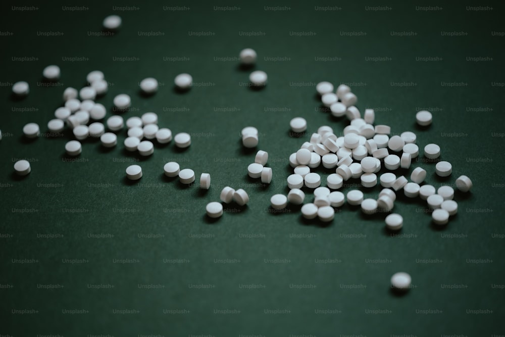 Un montón de píldoras blancas sentadas encima de una mesa verde