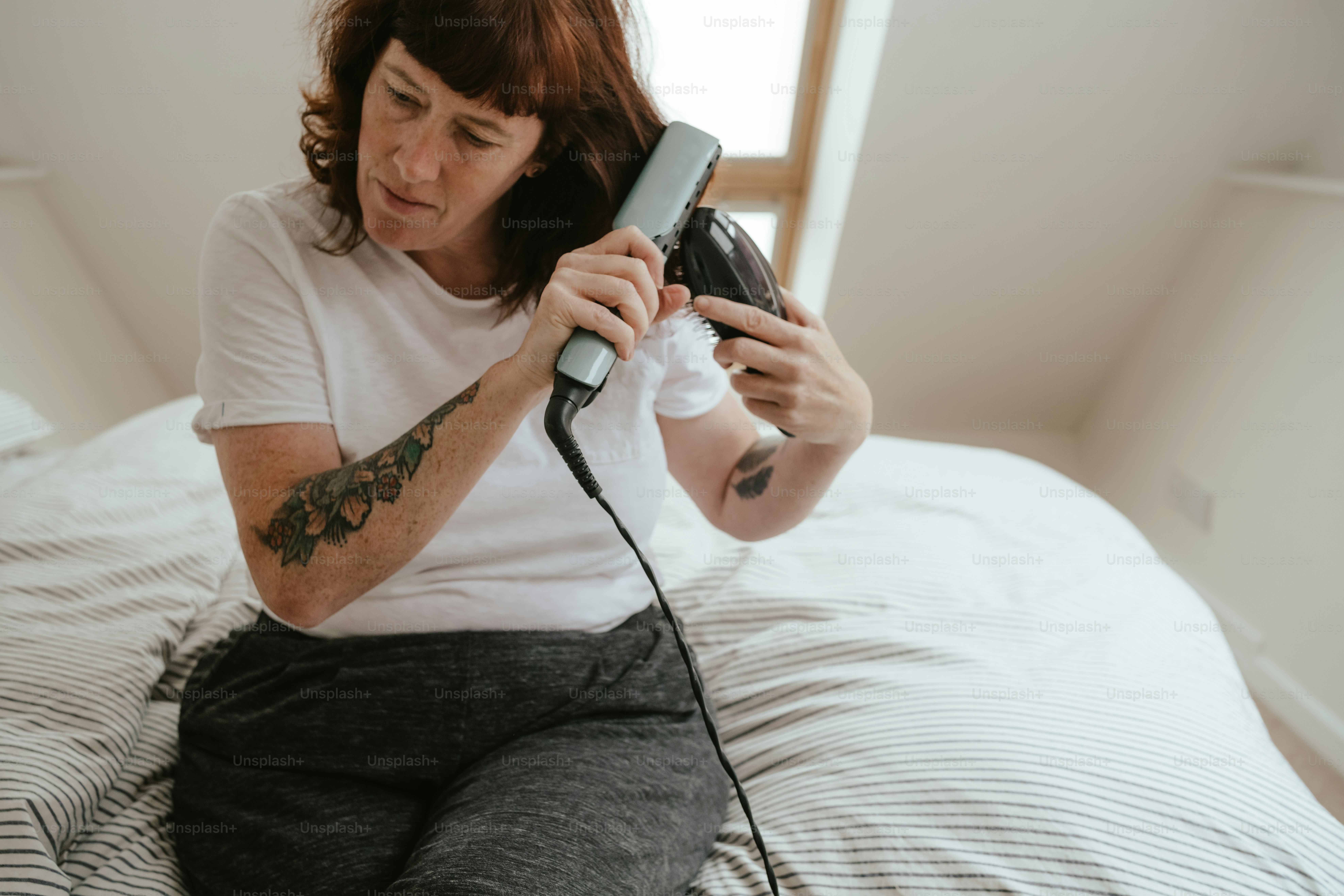 a woman sitting on a bed holding a hair dryer
