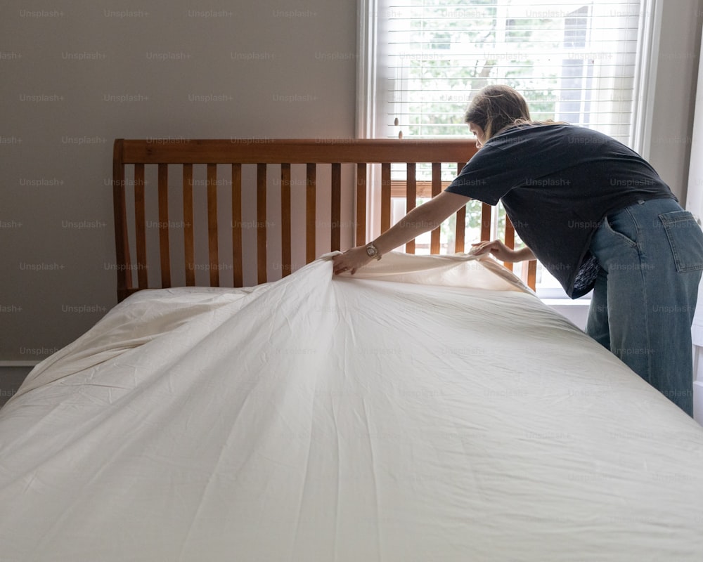 Una persona poniendo una sábana encima de una cama