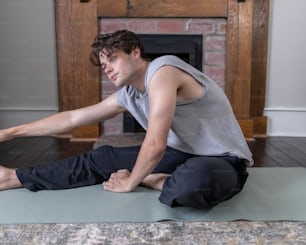 a man sitting on a yoga mat in front of a fireplace