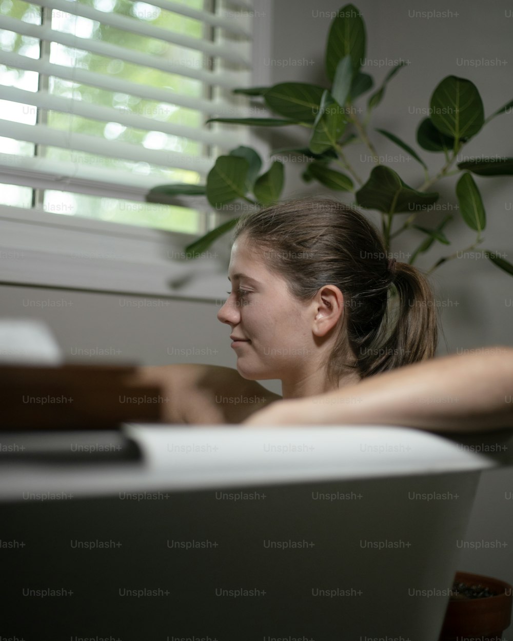 uma mulher sentada em uma banheira ao lado de uma janela