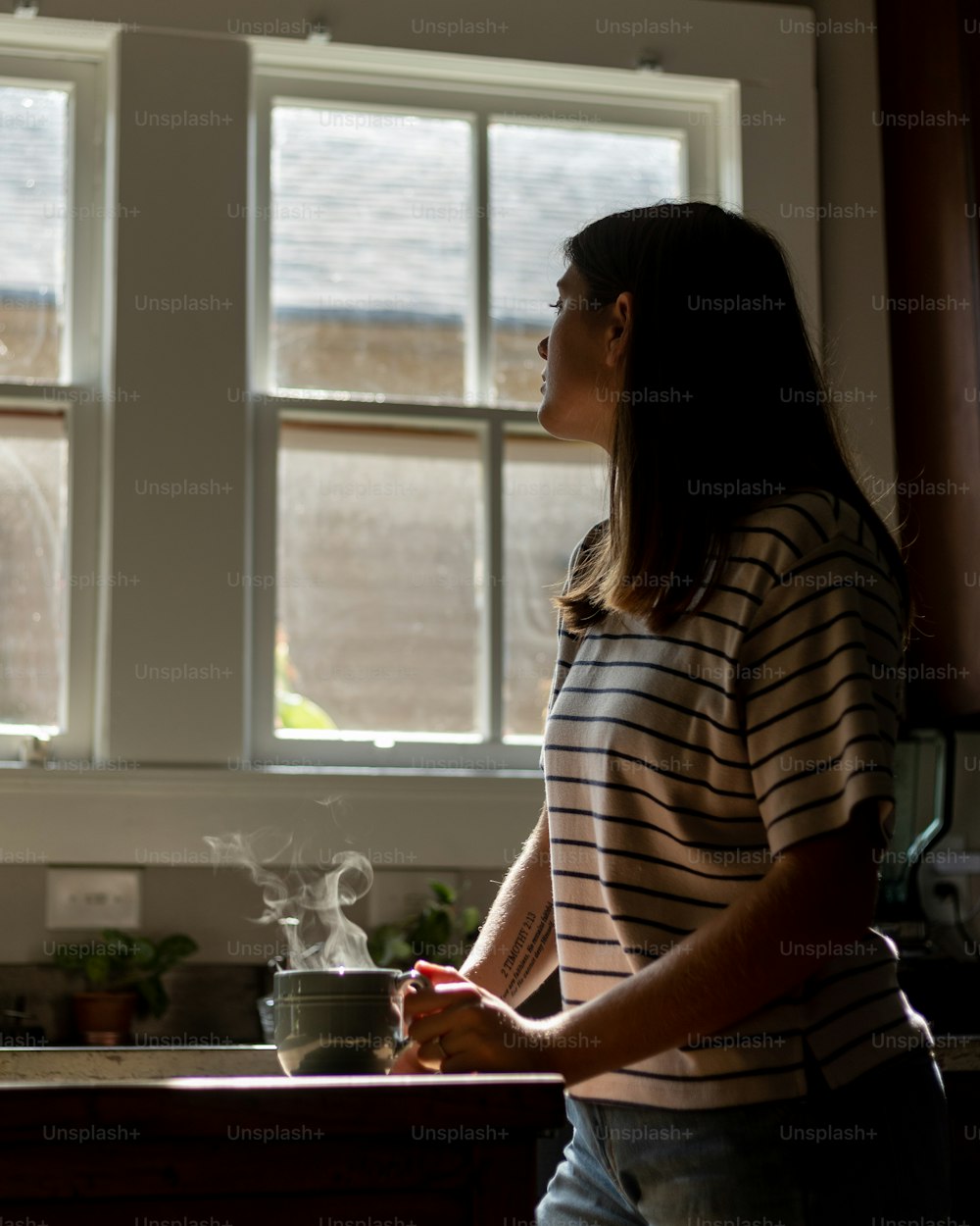 Une femme debout dans une cuisine à côté d’une fenêtre