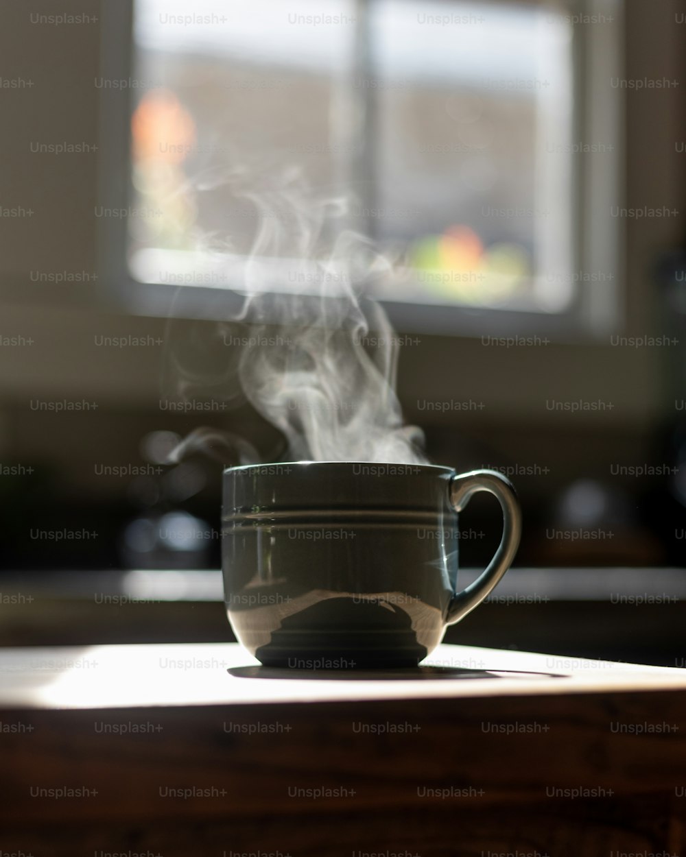 a steaming cup on a table with a window in the background