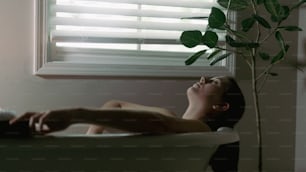 a woman laying in a bathtub next to a window