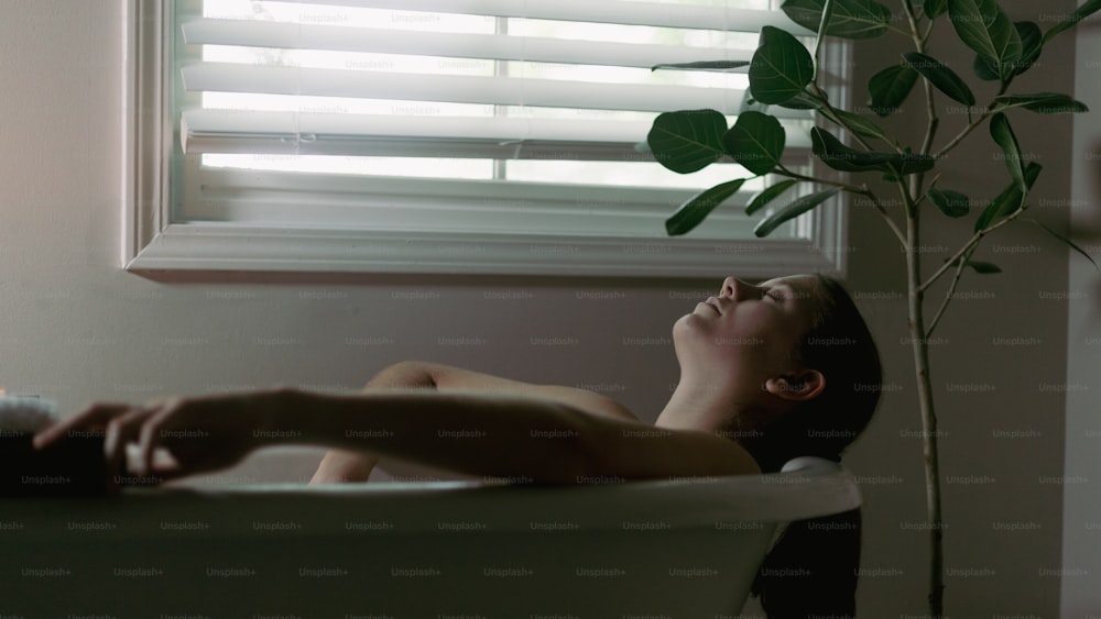 uma mulher deitada em uma banheira ao lado de uma janela