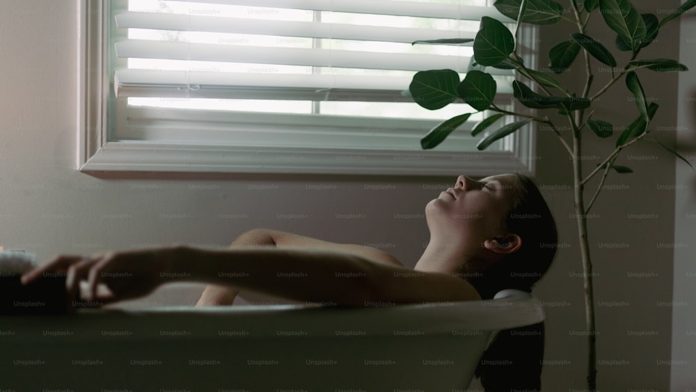 a woman laying in a bathtub next to a window