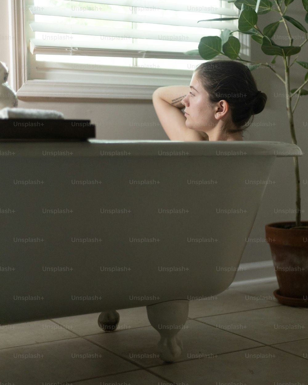 a woman sitting in a bathtub next to a plant