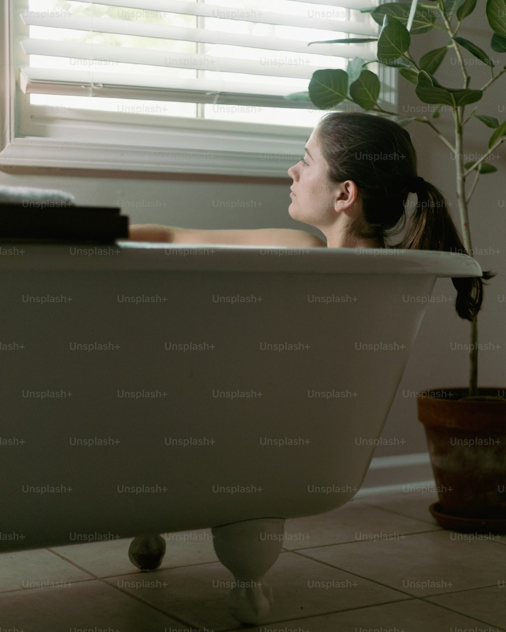 una donna seduta in una vasca da bagno accanto a una pianta