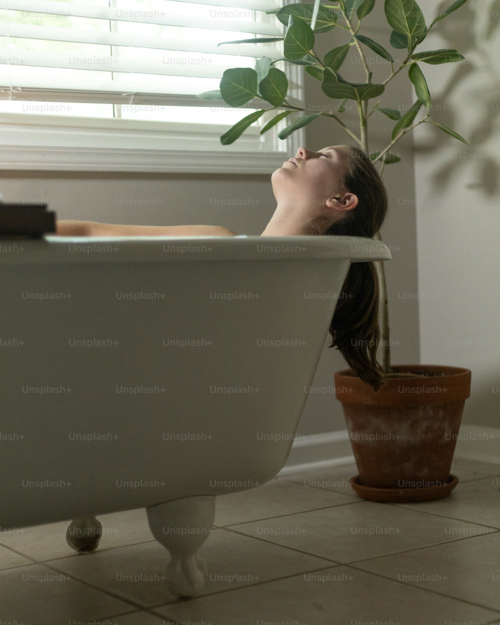 uma mulher deitada em uma banheira ao lado de um vaso de planta