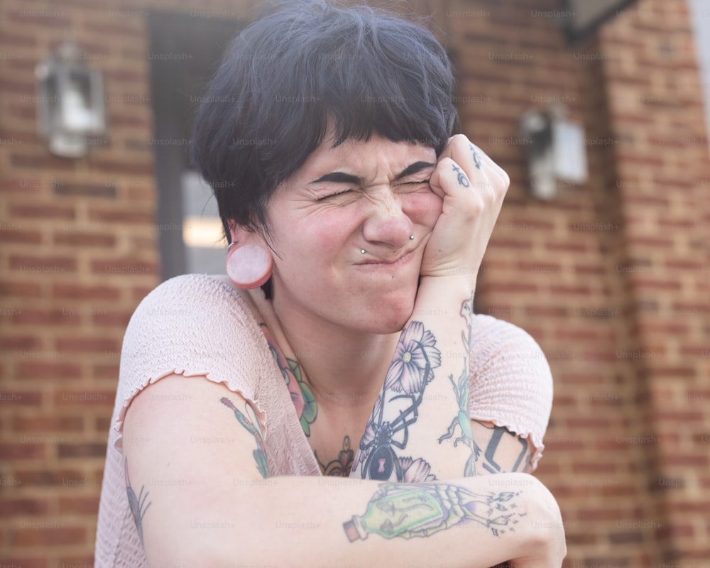 uma mulher com uma tatuagem no braço segurando a mão no rosto