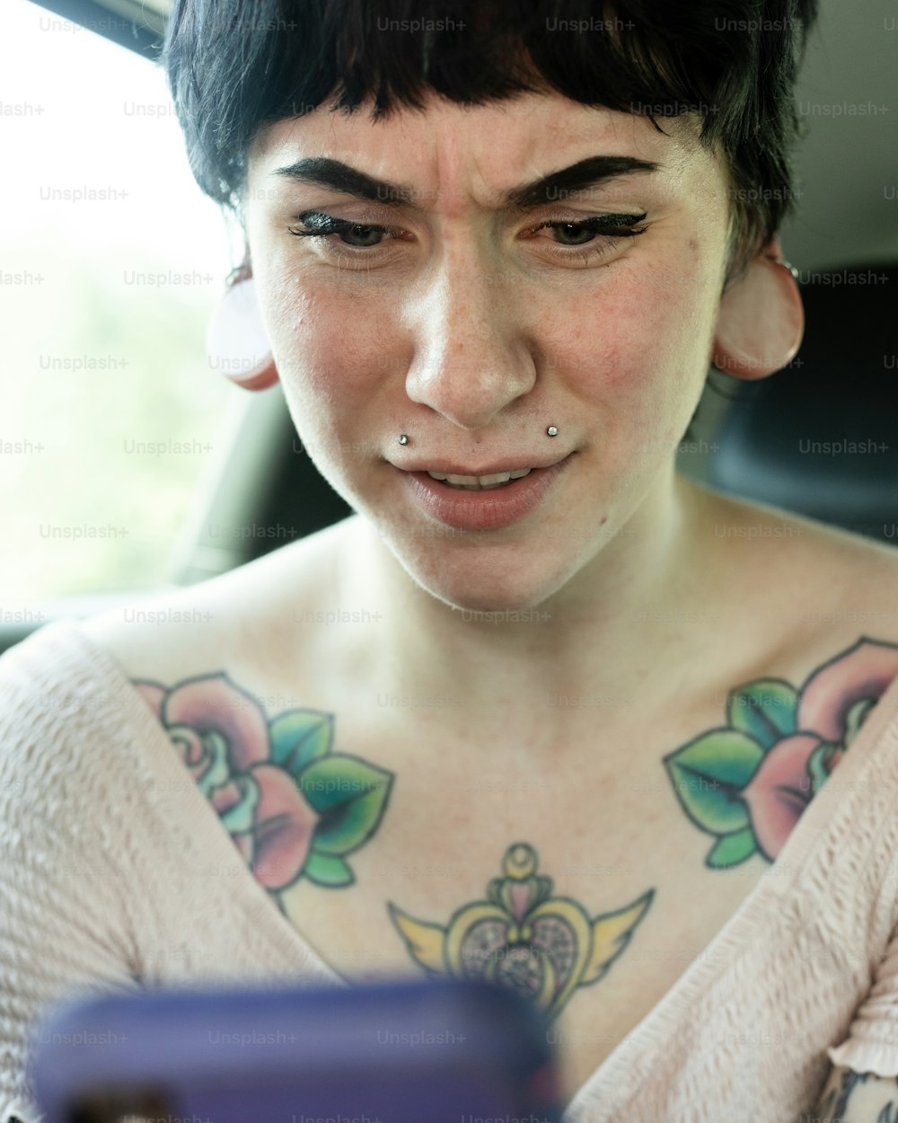 Eine Frau mit Tätowierungen auf der Brust schaut auf ein Handy