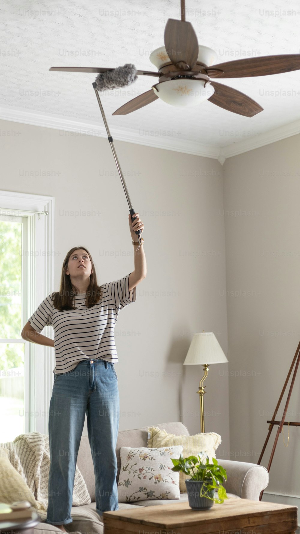 Une femme debout dans un salon tenant un ventilateur de plafond