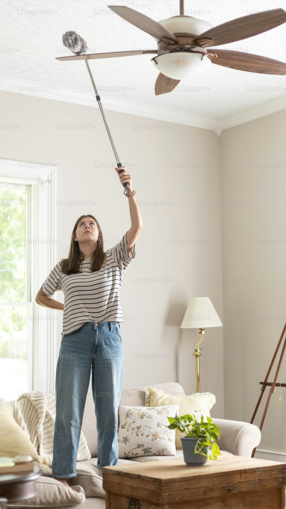a woman standing in a living room holding a ceiling fan