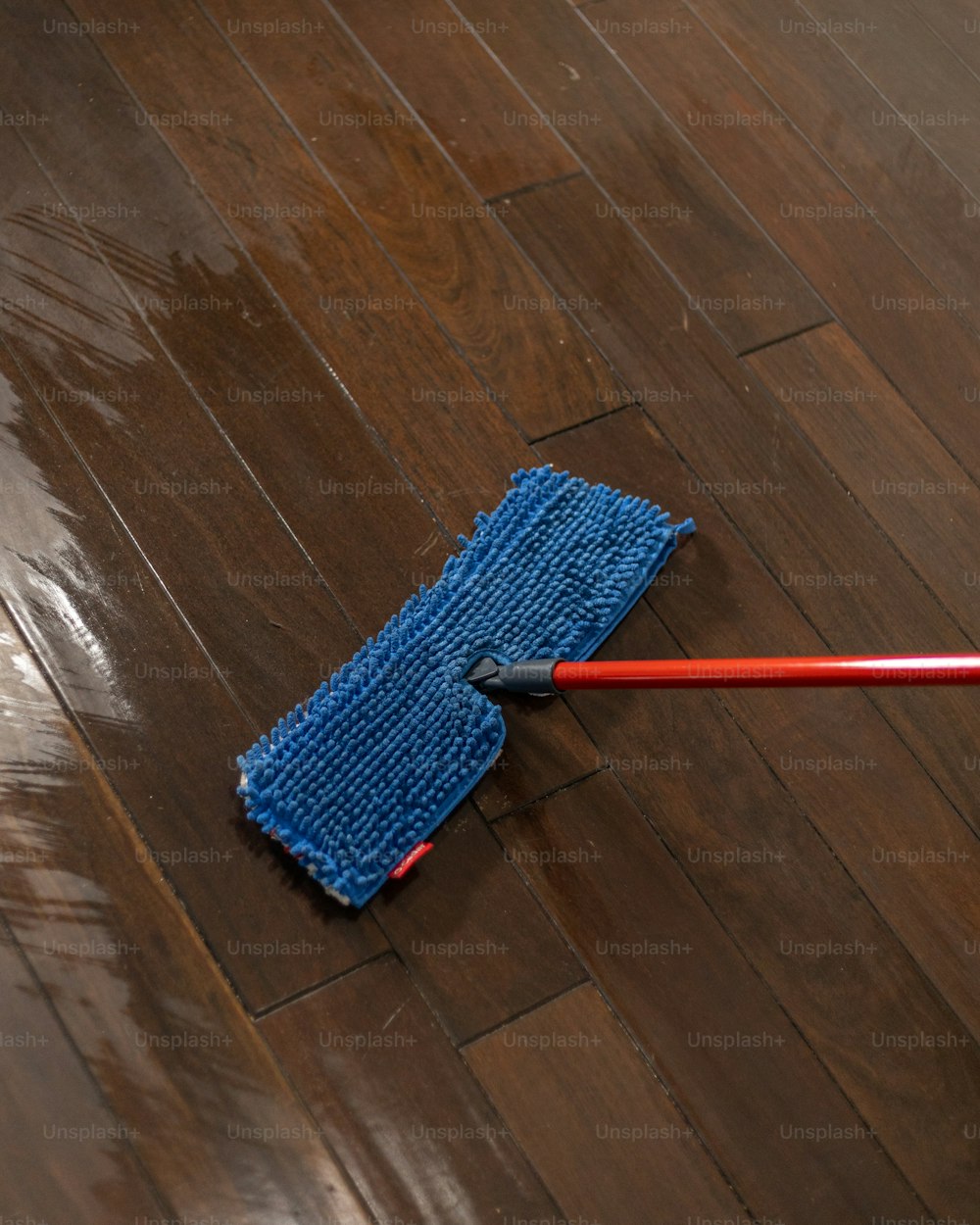 um esfregão azul com uma alça vermelha em um piso de madeira