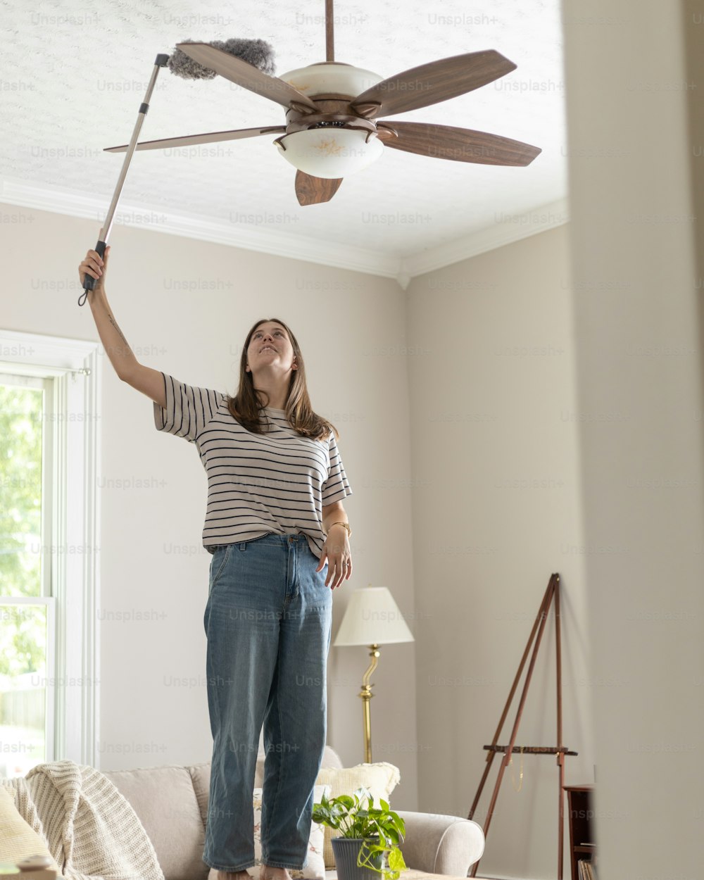 uma mulher em pé em uma sala de estar segurando um ventilador de teto