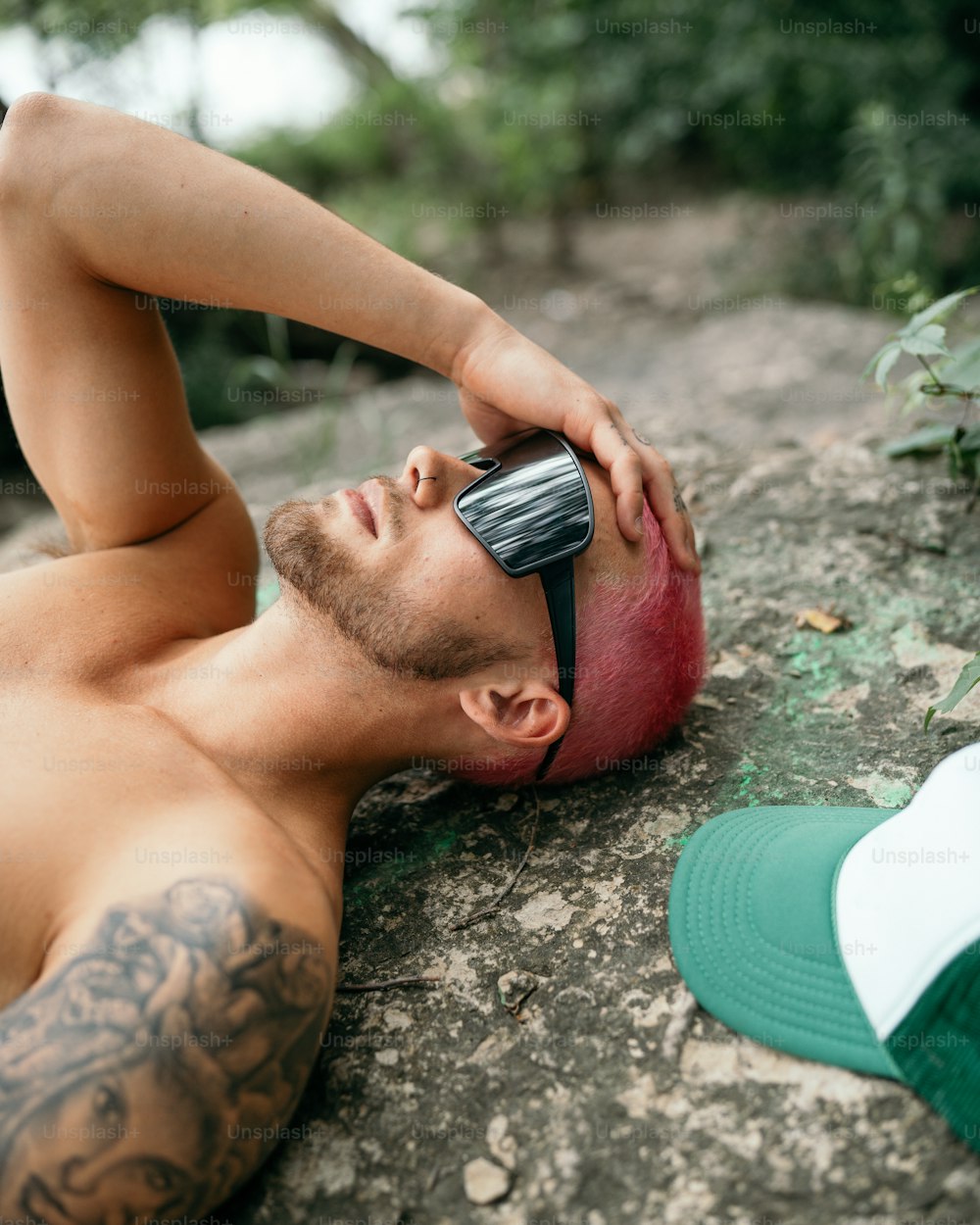 a shirtless man laying on a rock talking on a cell phone