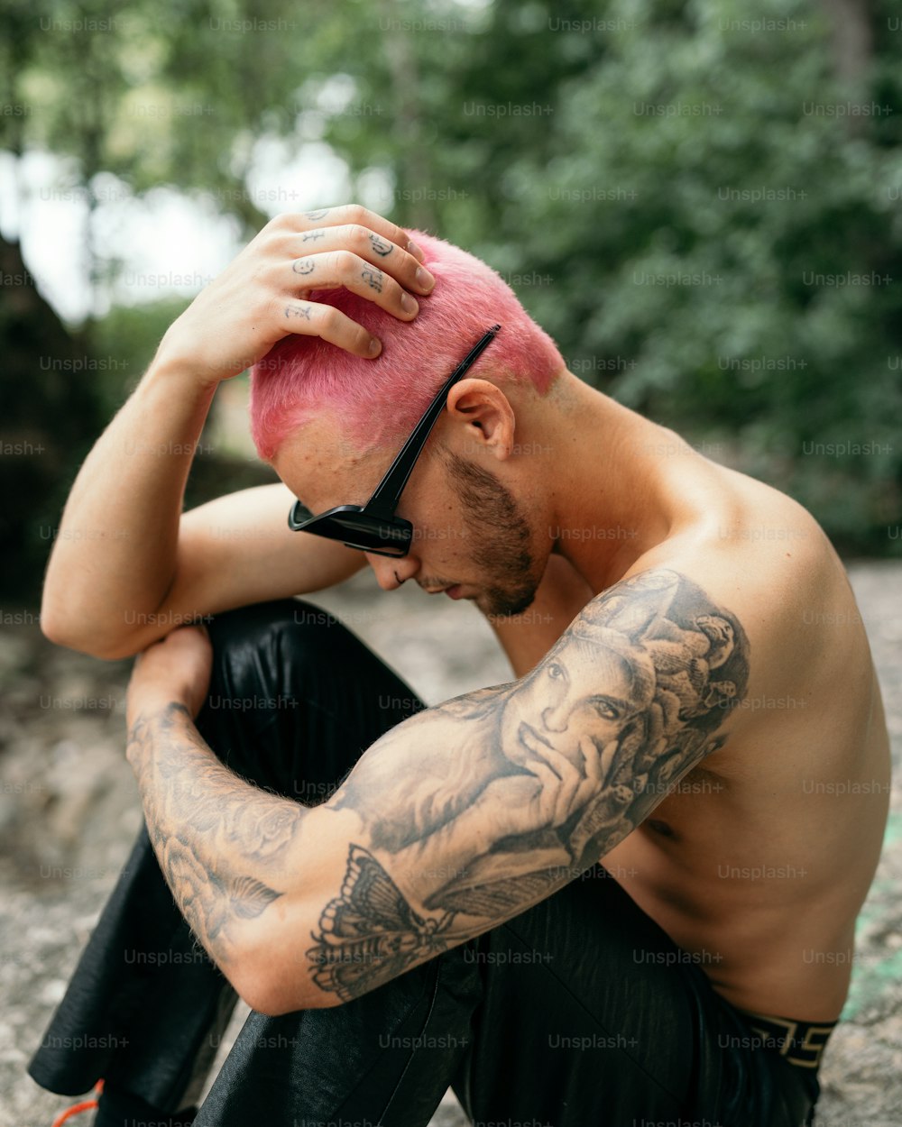 Un hombre con un mohawk rosa sentado en una roca