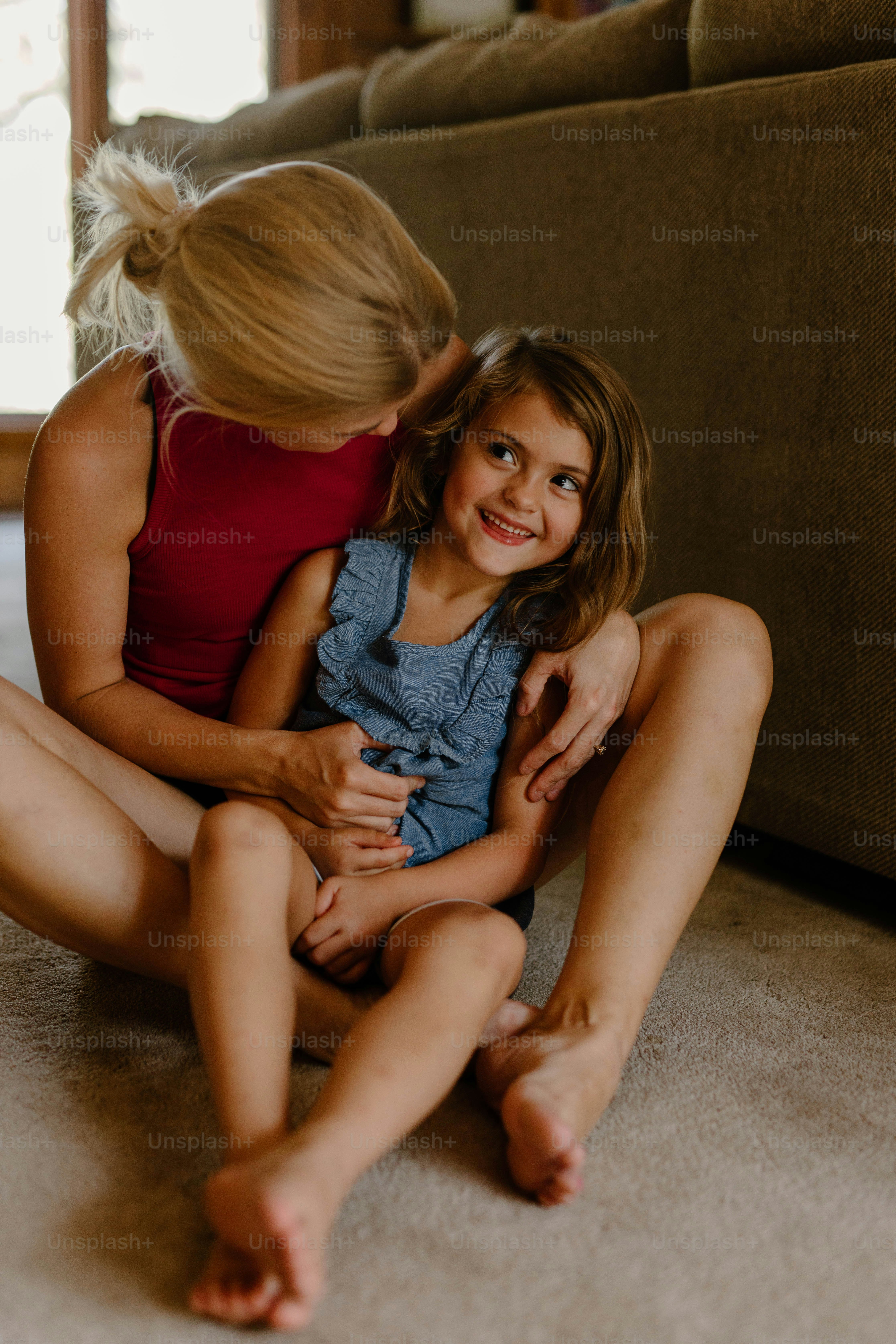 a woman sitting on the floor hugging a little girl