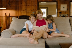uma mulher e duas meninas sentadas em um sofá lendo um livro