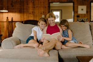 a woman and two girls sitting on a couch reading a book