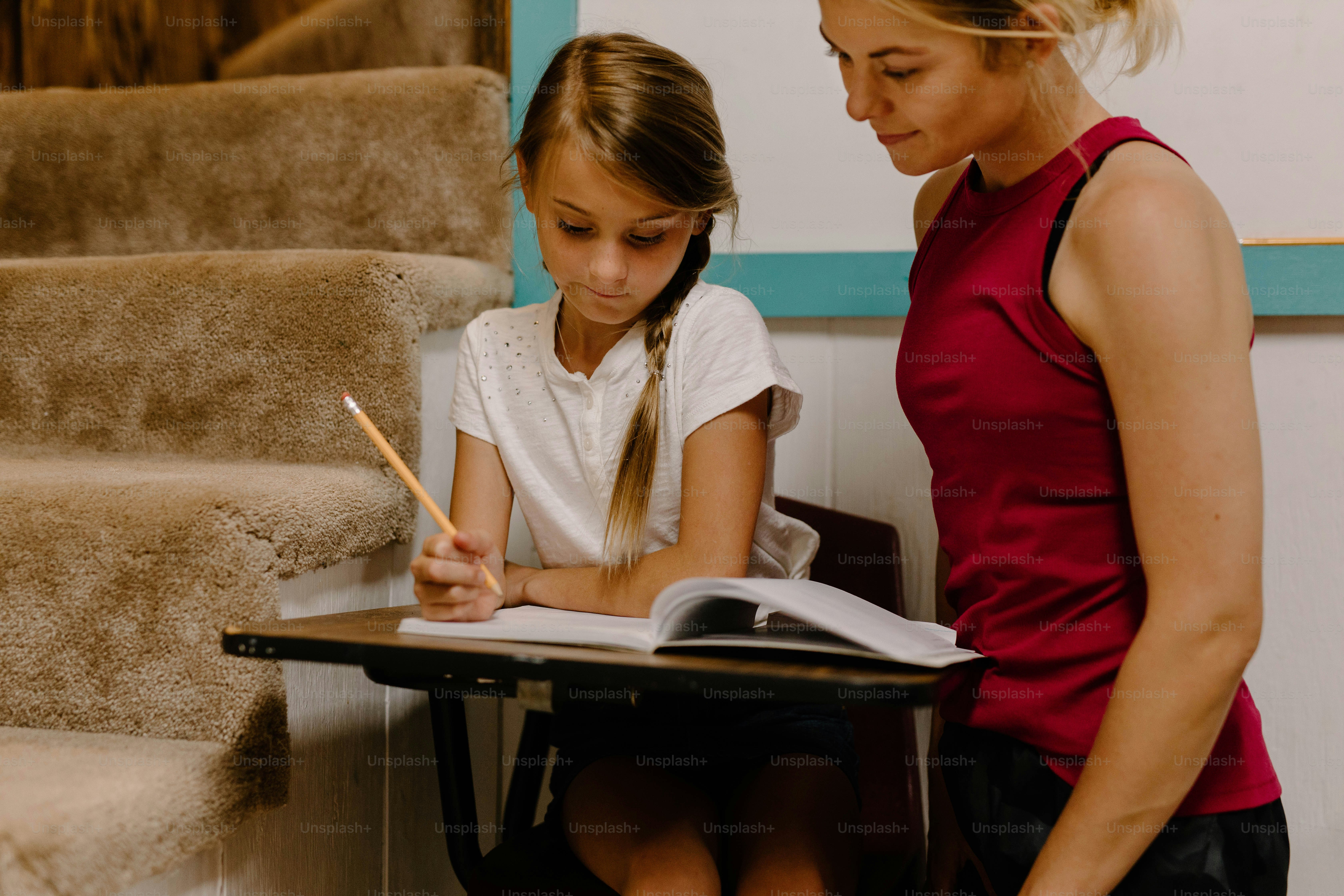 a woman and a girl sitting at a desk writing
